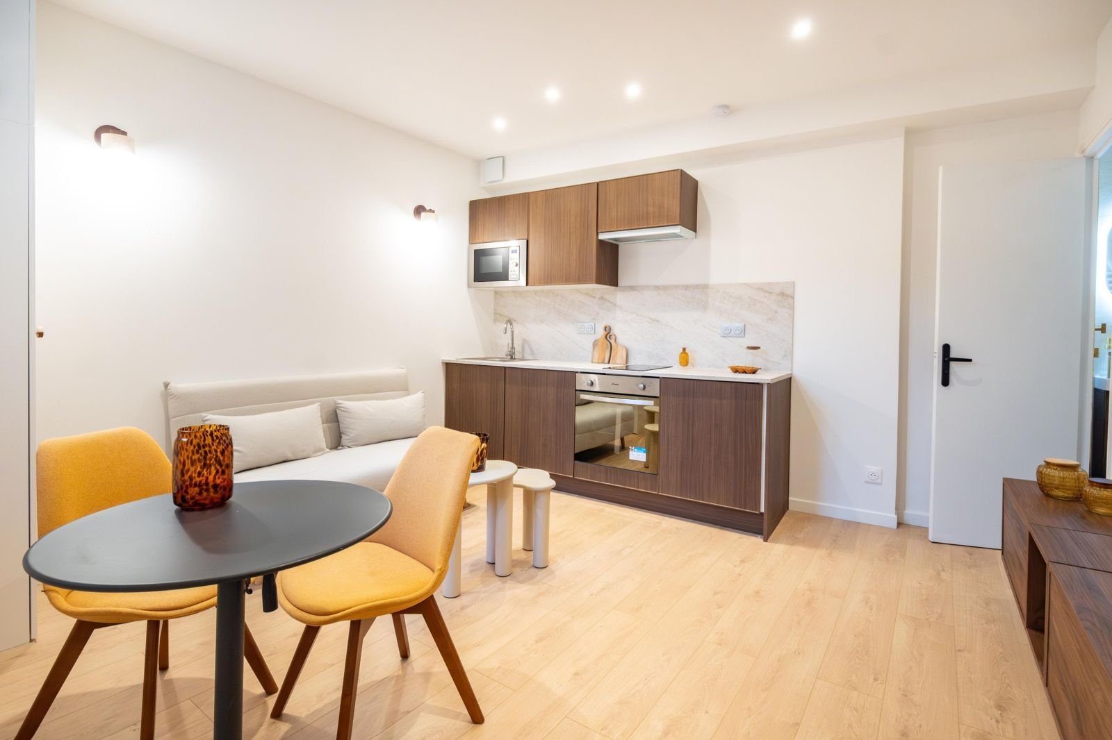 Studio rénové : parquet clair, kitchenette bois, chaises jaunes